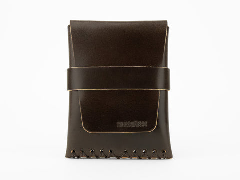 A dark brown leather pouch with visible stitching at the bottom and a horizontal strap across the front, displayed upright on a white background. The word BLVKRVK is embossed on the front flap.