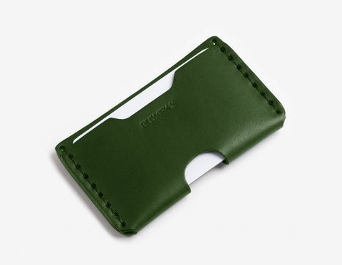 A slim, green leather cardholder with visible stitching and two slots holding white cards, placed on a plain white background.
