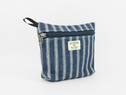 A denim striped canvas pouch with zipper closure on a neutral background. It features a cream woven tag that reads "Billykirk made in america since 1999".