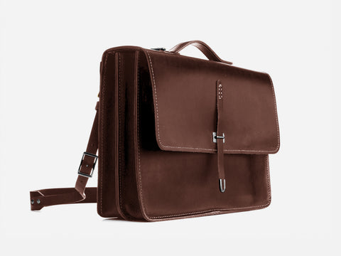 A brown leather briefcase with a top handle, front flap, silver buckle closure, and an adjustable shoulder strap, shown against a plain white background.