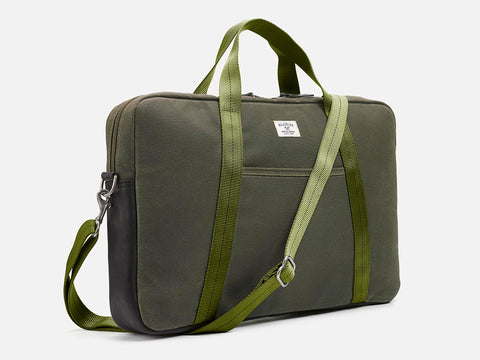A green canvas laptop bag with dual handles, a detachable shoulder strap, and a small white label on the front. The bag has a rectangular shape and appears to be sturdy and minimalist in design.