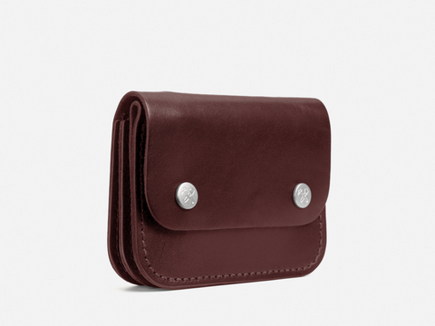 A small, dark brown leather wallet with two silver snap buttons on the front, shown standing on a white background.