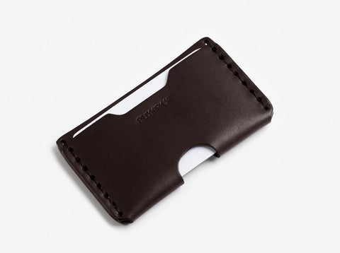 A dark brown leather wallet with visible stitching along the edges, holding two white cards, and featuring a small curved cutout on one side.