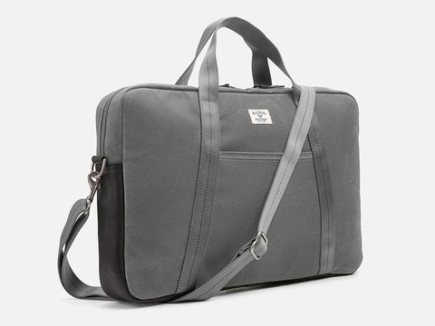 A gray fabric laptop bag with a zipper closure, two short carrying handles, an adjustable shoulder strap, and a small white label on the front. The bag is photographed against a plain white background.