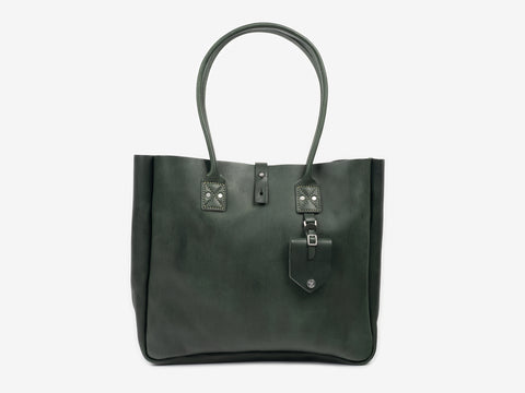 Front view of a medium-sized pine leather tote with handles for your shoulder. The tote features a removable luggage tag below one of the handles. The bag is set against a neutral background.
