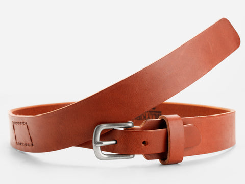 A tan leather belt with a silver buckle, coiled loosely against a white background. The belt features a stitched rectangular detail near the buckle.