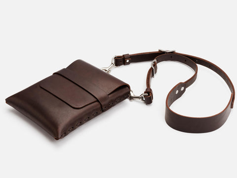 A dark brown leather crossbody bag with a front pocket and a long, adjustable strap, displayed against a white background.