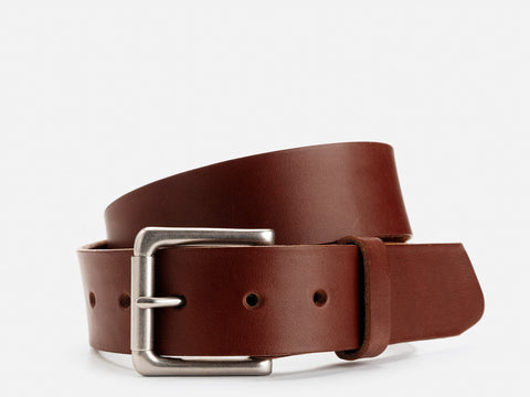A brown leather belt with a silver rectangular buckle is coiled on a white background. The belt has evenly spaced holes and a simple, classic design.