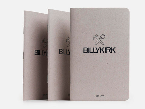 Three gray Billykirk notebooks stand upright in a row. Each has the Billykirk logo with a hammer and mallet above the brand name, and EST. 1999 printed at the bottom on a plain background.
