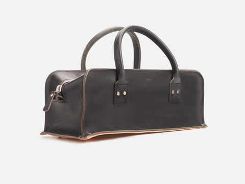 A 3/4 view of a black leather tool bag with rivet reinforced corners set in a white background