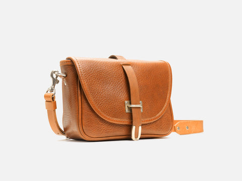 A small, brown leather crossbody bag with a flap closure, silver buckle detail, and an adjustable strap, displayed on a plain white background.