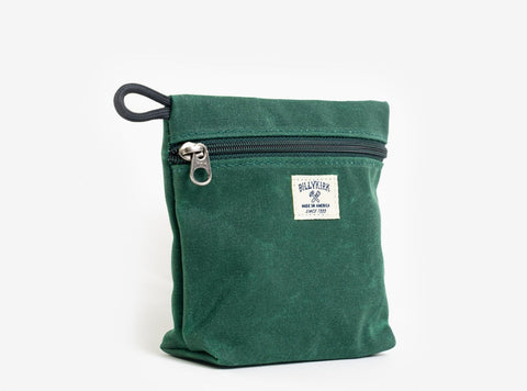 A green waxed canvas pouch with zipper closure on a neutral background. It features a cream woven tag that reads "Billykirk made in america since 1999".