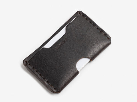 A slim, dark brown leather card holder with visible stitching and a single card partially inserted into one of the open slots.