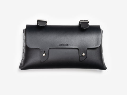 A black leather clutch bag with a flap closure, silver rivet details, and two buckle straps on top, set against a white background.