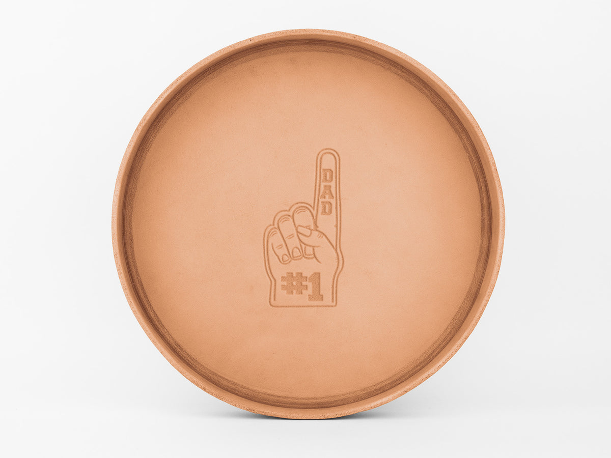 Round tan tray with an engraved image of a foam finger in the center, displaying the words “DAD” on the finger and “#1” on the palm, against a plain white background.