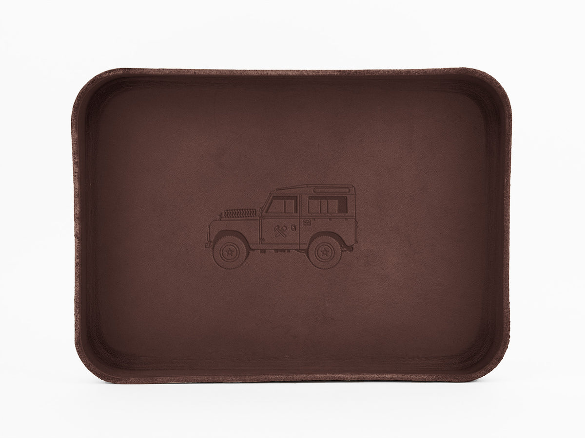 A rectangular, brown tray with rounded edges, featuring an embossed outline of a classic off-road vehicle in the center on a plain white background.