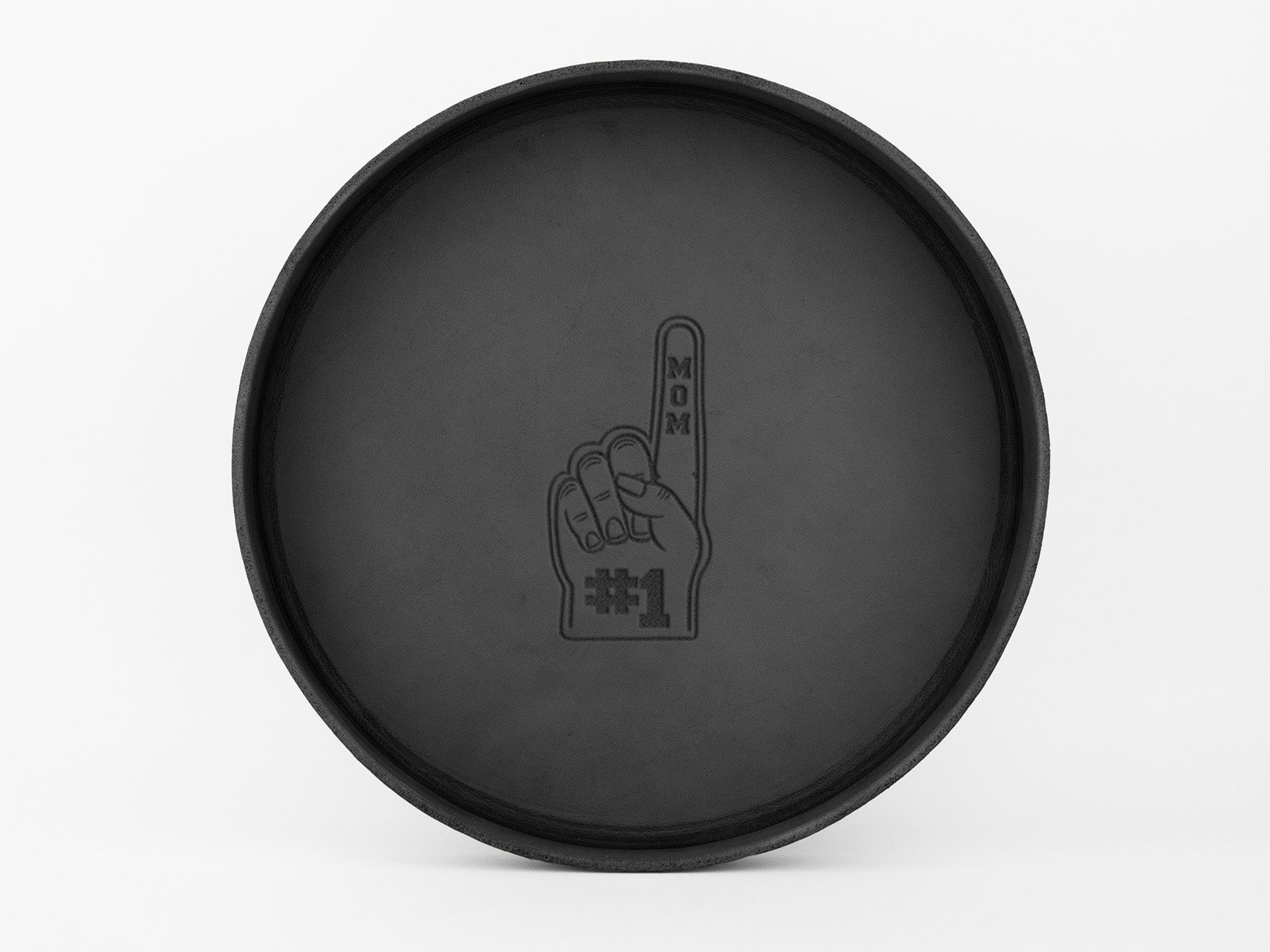A black circular tray with an illustration of a foam finger in the center, displaying the words MOM #1. The background is plain white.
