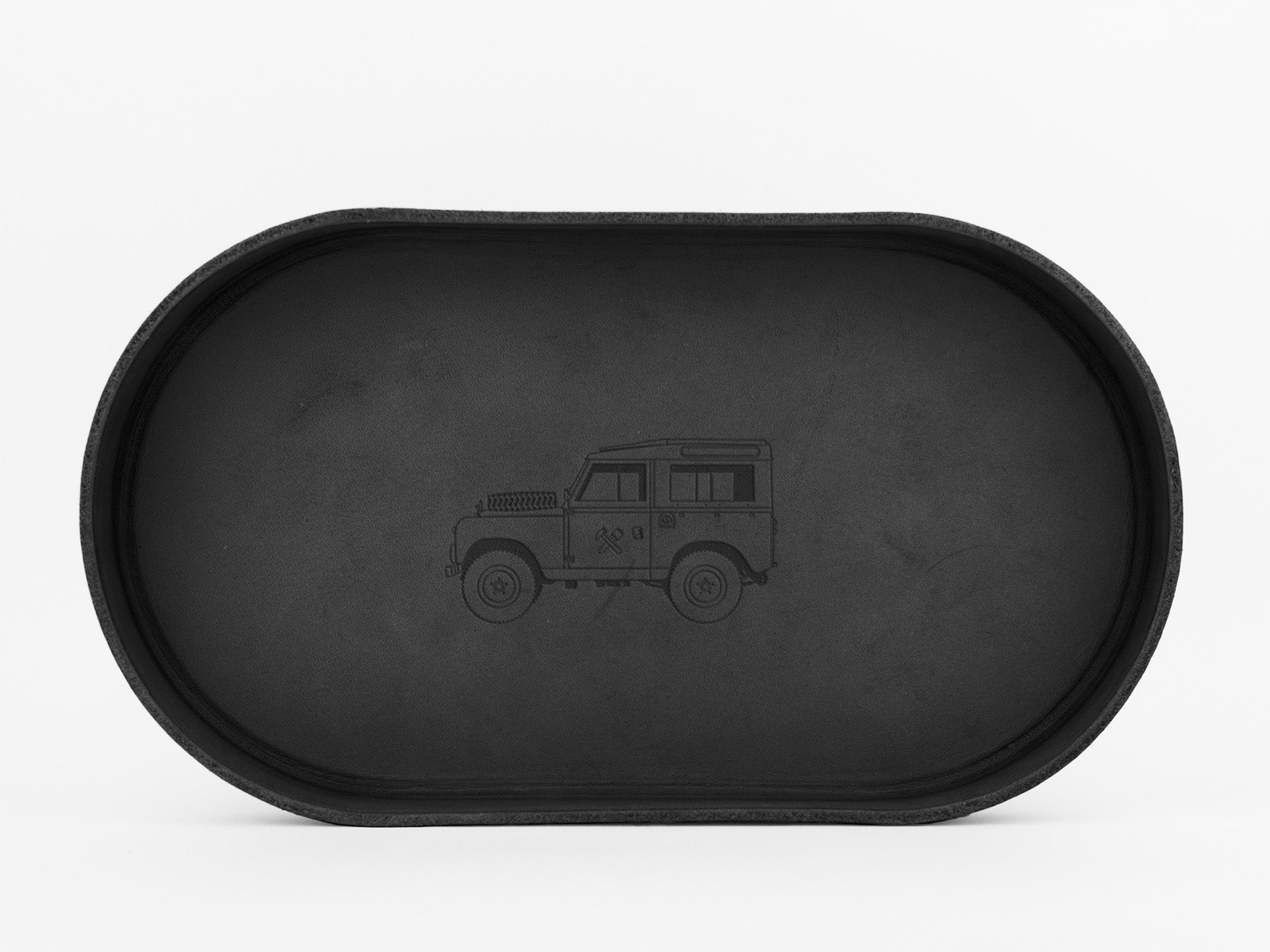 A black, oval-shaped tray with an outline drawing of a classic SUV, similar to a Land Rover, engraved in the center. The background is plain white.