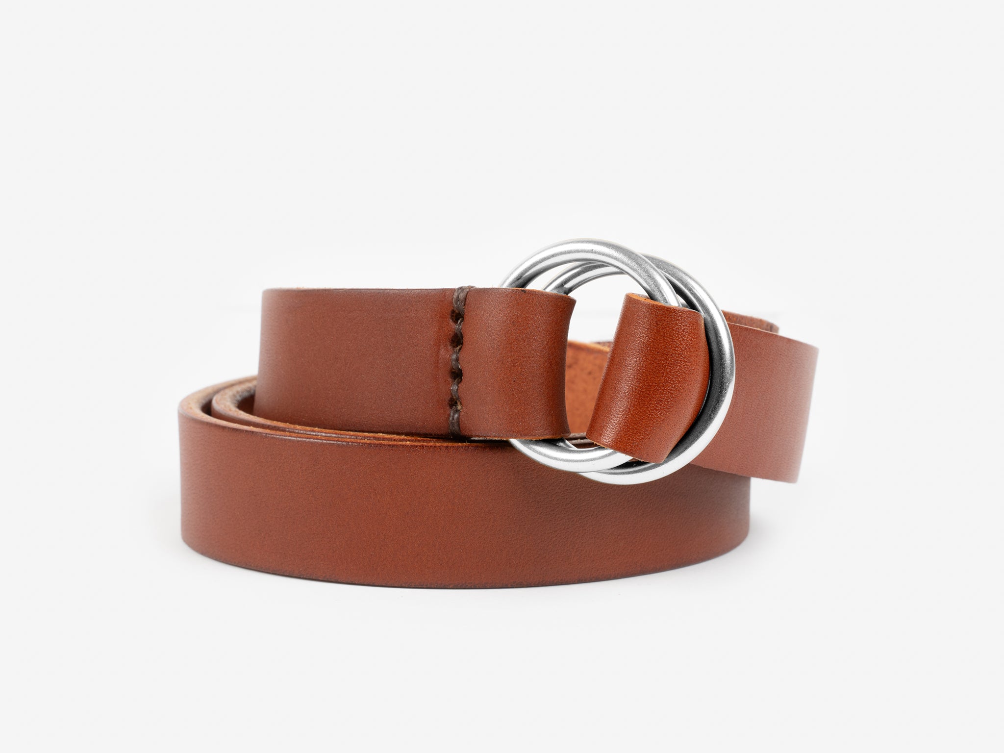 A tan leather belt with stitched detailing near the end, featuring a double silver ring buckle, displayed coiled on a white background.
