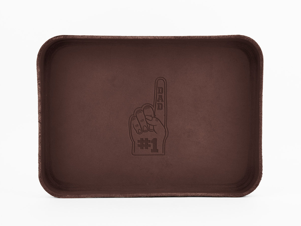 A rectangular brown tray with an engraved graphic of a raised hand showing the index finger, reading “DAD #1” on the palm and finger. The background is plain white.