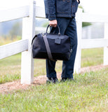 Person holding a black carryall bag outdoors near a white fence