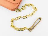 A gold chain with a clasp on one end and a hook on the other is attached to a tan leather wallet, displayed on a white background.