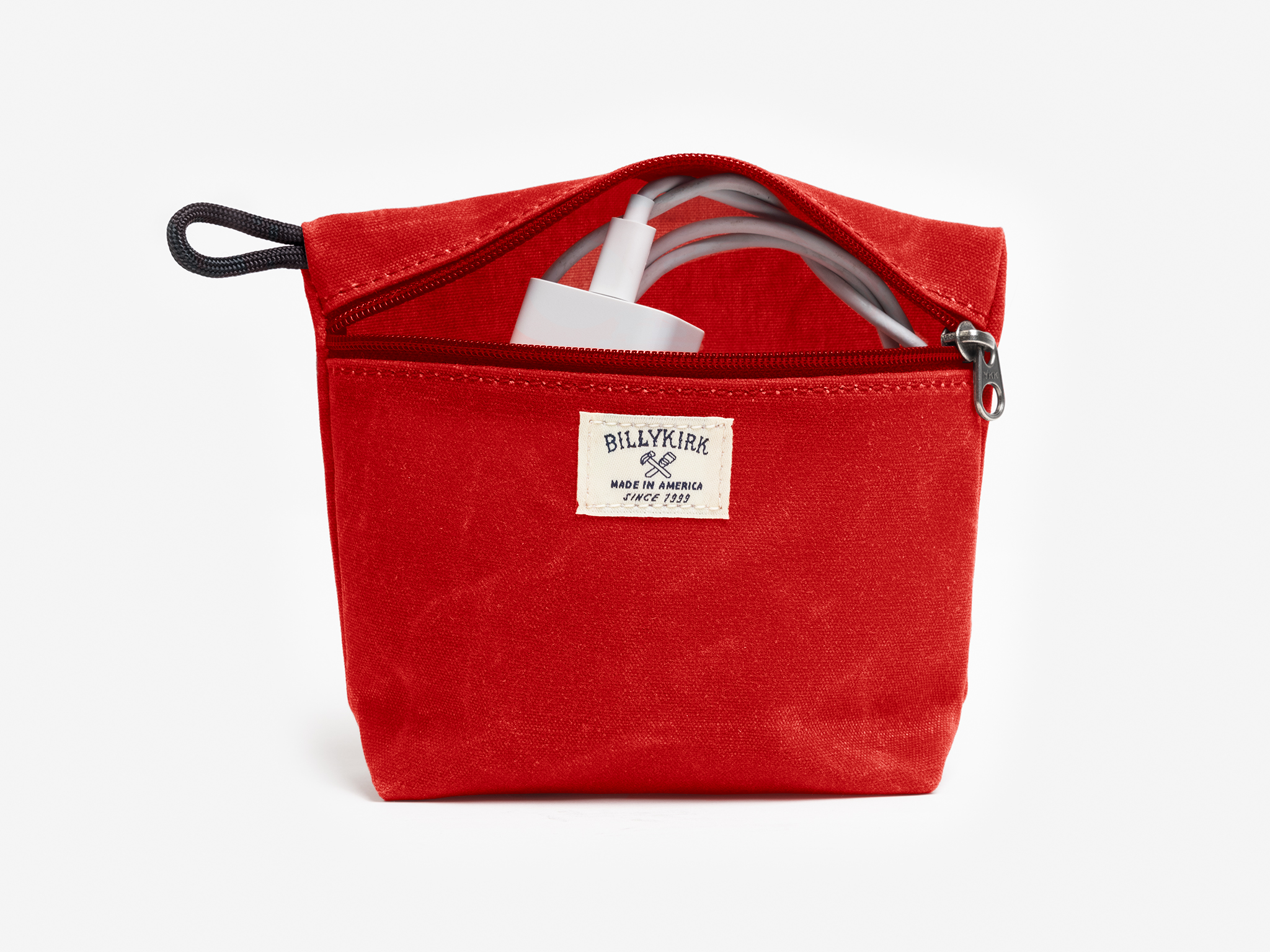 A red waxed canvas pouch with zipper closure on a neutral background. It features a cream woven tag that reads "Billykirk made in america since 1999" and has a white cord coming from the pouches opening.