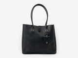 Front view of a medium-sized black leather tote with handles for your shoulder. The tote features a removable luggage tag below one of the handles. The bag is set against a neutral background.