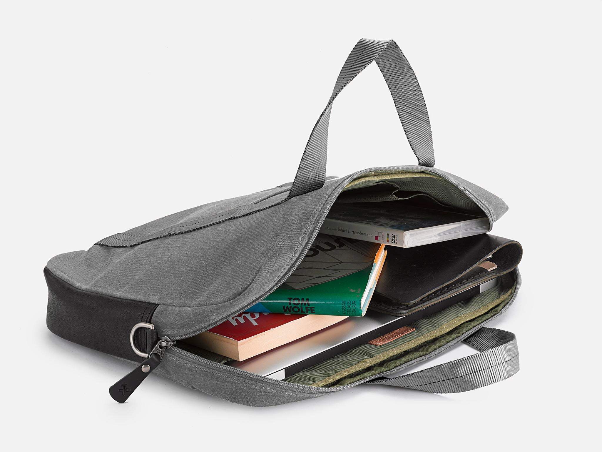 A gray fabric briefcase lies open, revealing books, a notebook, and a tablet inside. The bag has two handles and is placed on a white background.