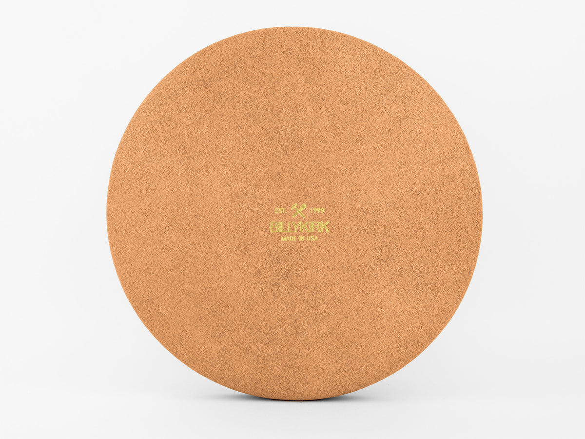 A round, flat cork mat with a light brown color. The center features yellow text that reads, EST 1999 FLÎYANK MADE IN USA, against a plain white background.