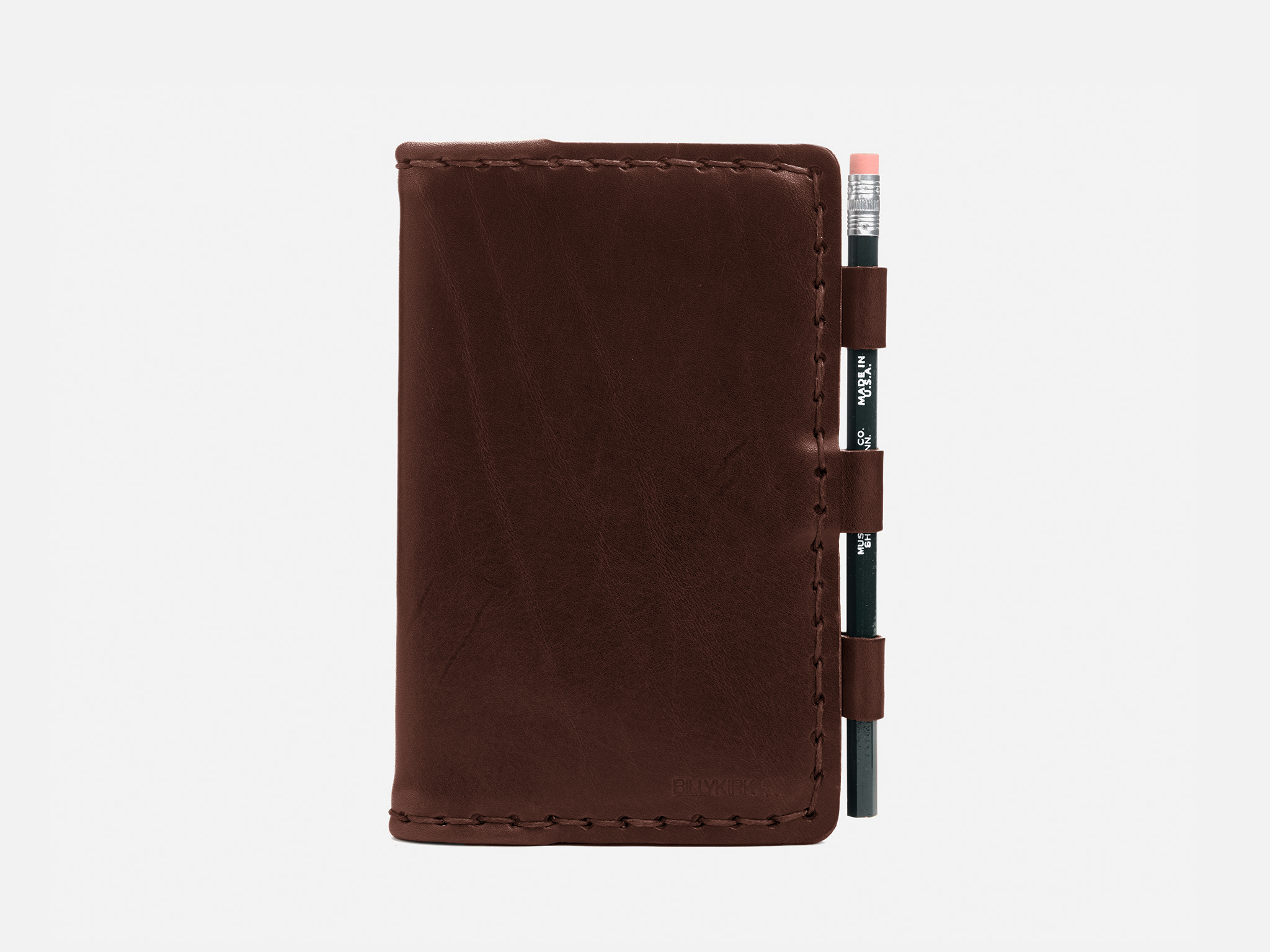 A brown leather notebook cover with visible stitching, holding a small black pencil with a pink eraser in three leather loops on the right side, displayed against a plain white background.