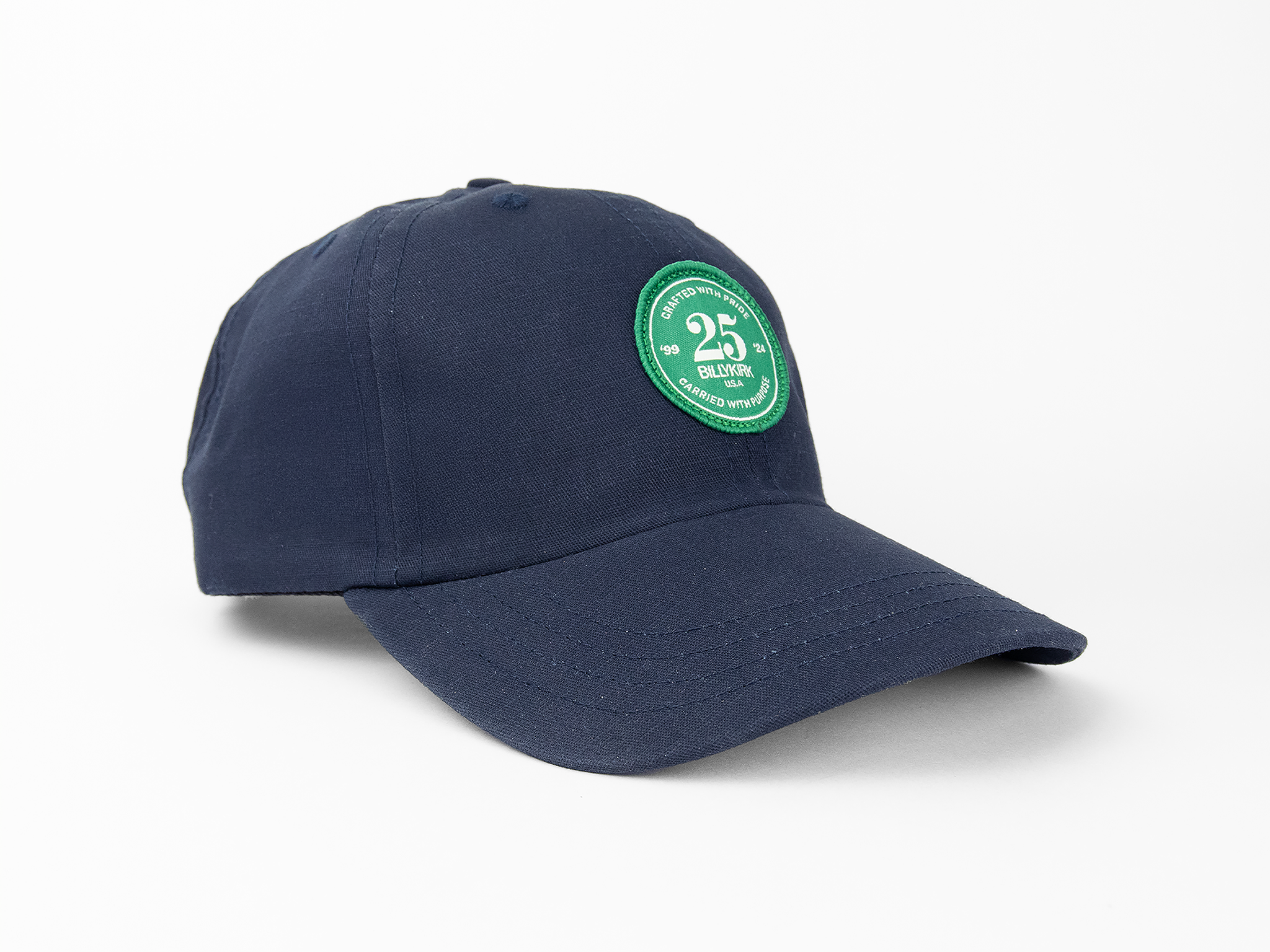 A navy blue baseball cap featuring a green and white circular patch on the front that reads “25th Billykirk” among other text.