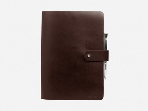 A closed, dark brown leather notebook with a buttoned strap and a silver pen attached at the side, set against a plain white background.