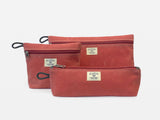 Three different sized nantucket red canvas bags with zipper closures arranged together on a neutral background.