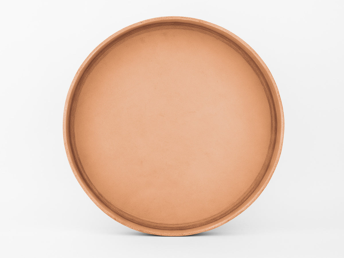 A round, flat, unadorned terracotta plate or tray is centered against a plain white background.