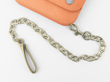 A brass chain with a hook and clasp is attached to an orange leather wallet, resting on a white surface.