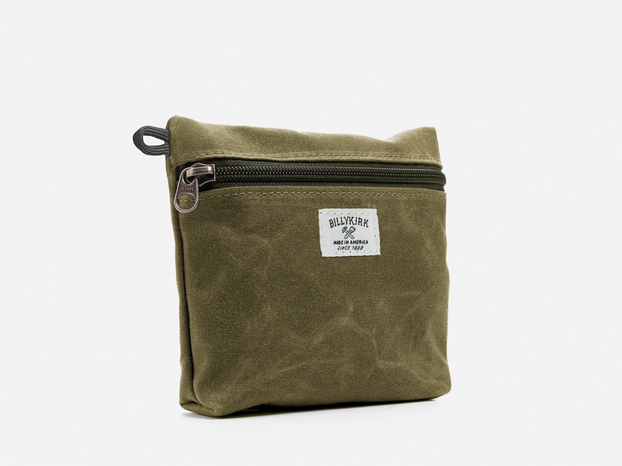 An olive waxed canvas pouch with zipper closure on a neutral background. It features a cream woven tag that reads "Billykirk made in america since 1999".