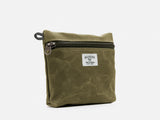 An olive waxed canvas pouch with zipper closure on a neutral background. It features a cream woven tag that reads "Billykirk made in america since 1999".