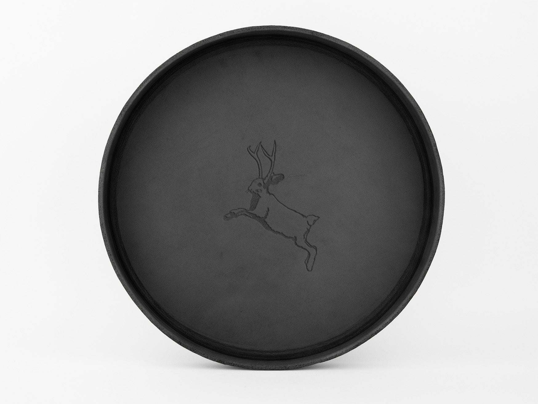 A round, black tray with a simple line drawing of a leaping jackalope—a rabbit with antlers—in the center, set against a plain white background.