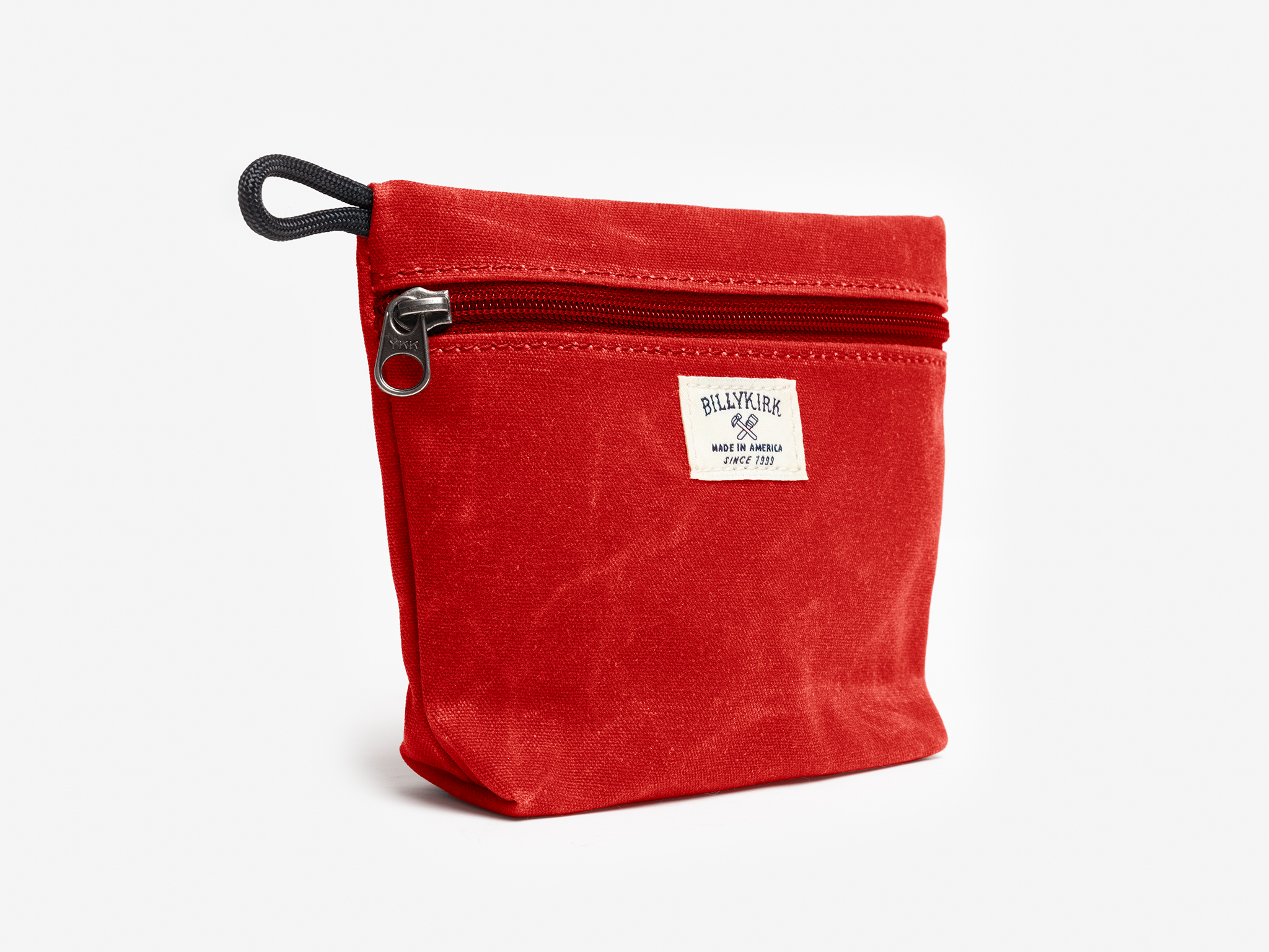 A red canvas pouch with zipper closure on a neutral background. It features a cream woven tag that reads "Billykirk made in america since 1999".