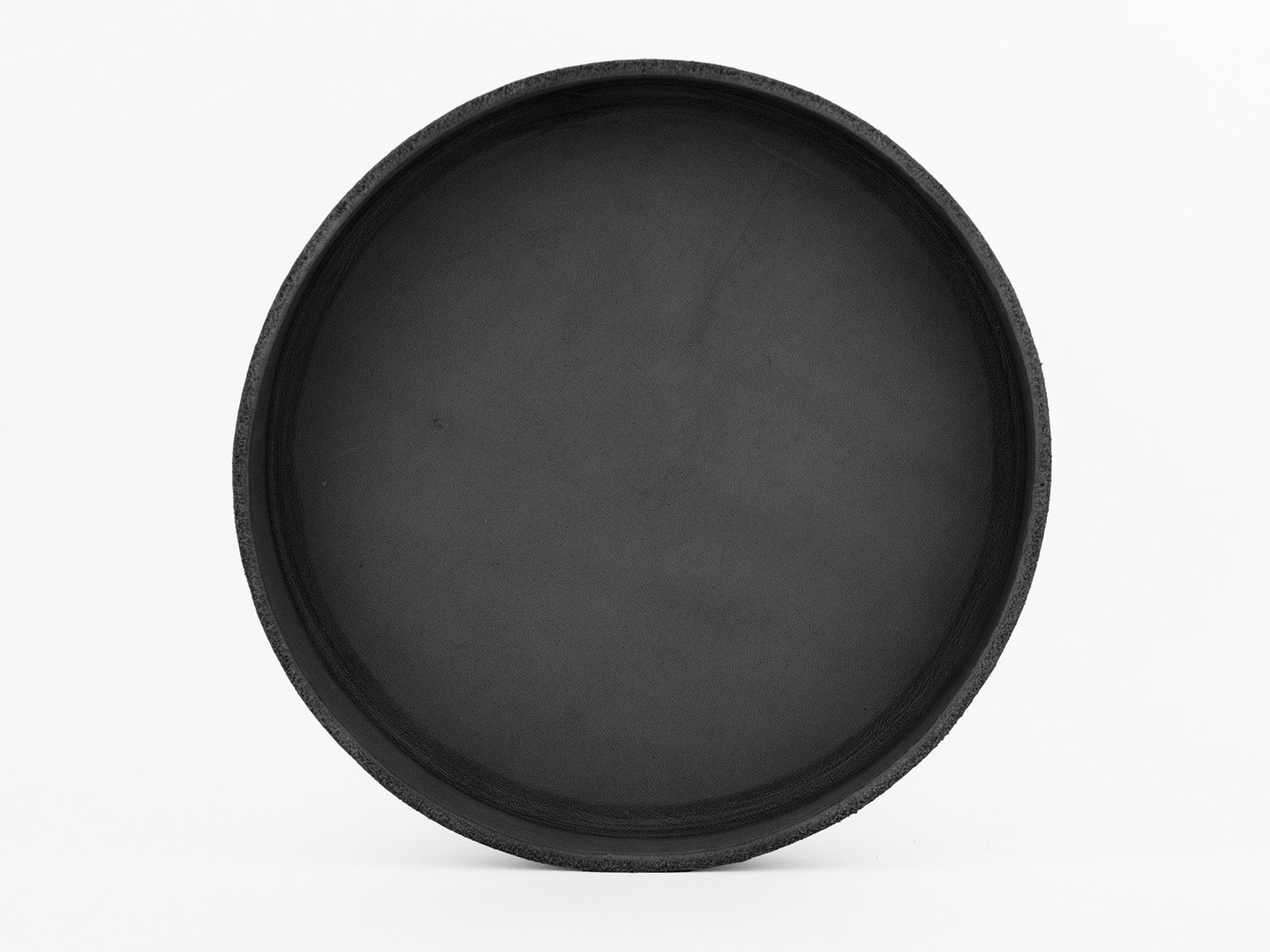 A round, black, empty tray or shallow dish is centered against a plain white background. The surface appears smooth and matte, with subtle texture along the rim.