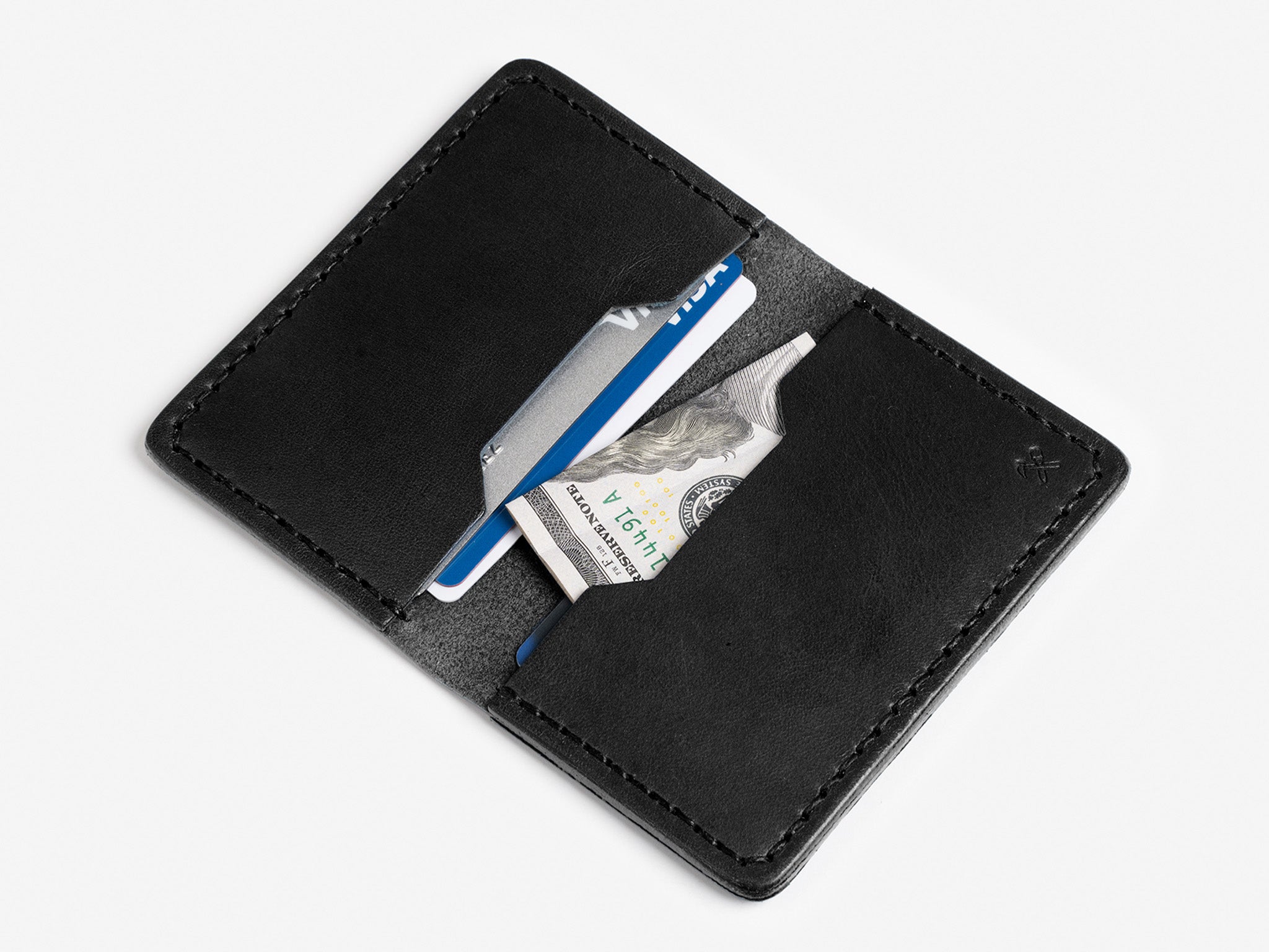 A black leather wallet open on a white surface, holding a blue credit card, a gray card, and a folded U.S. dollar bill in its compartments.