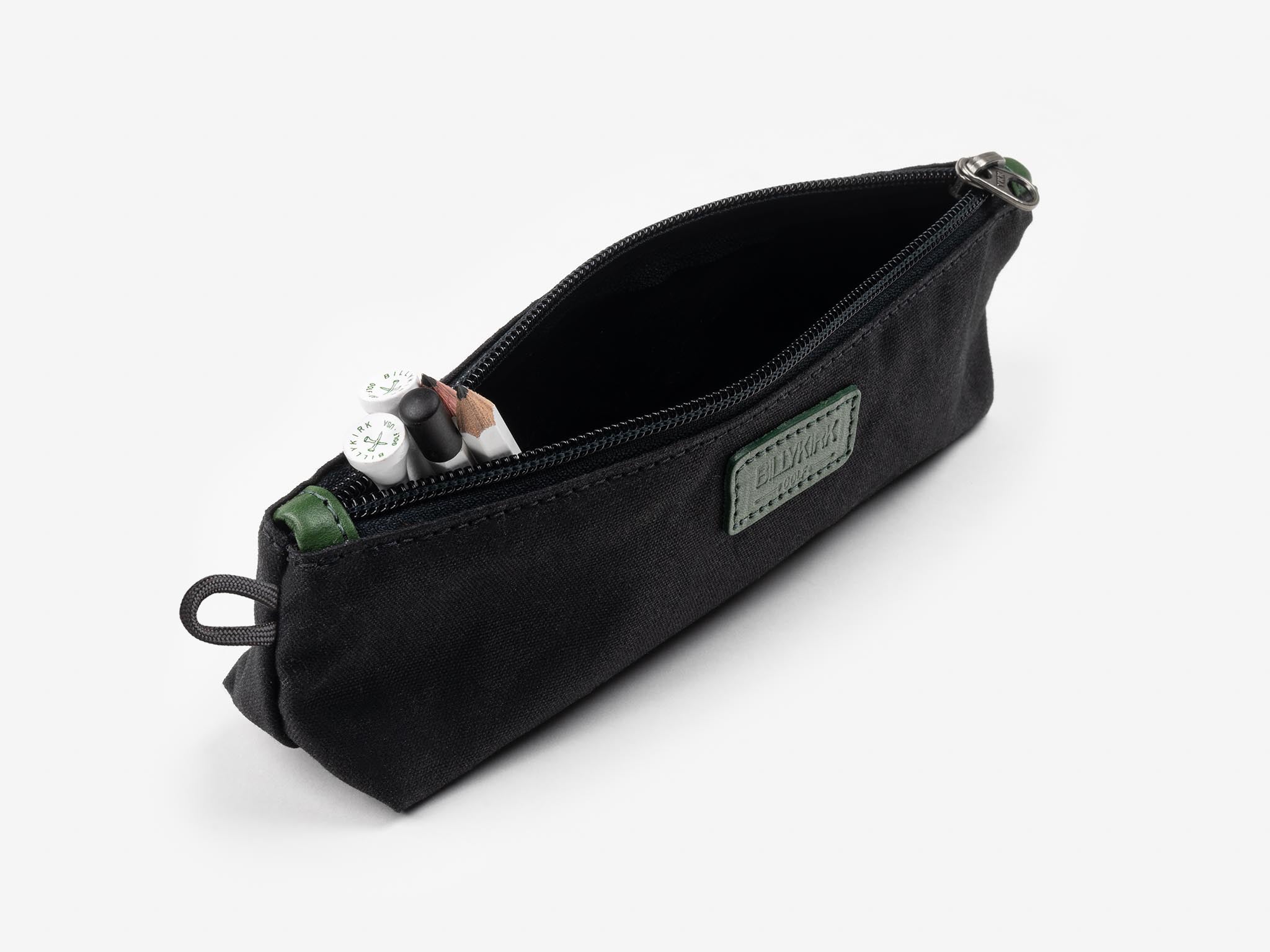 Black zippered pencil case with a green patch, partially unzipped to reveal a few pens and pencils inside, photographed on a plain white background.