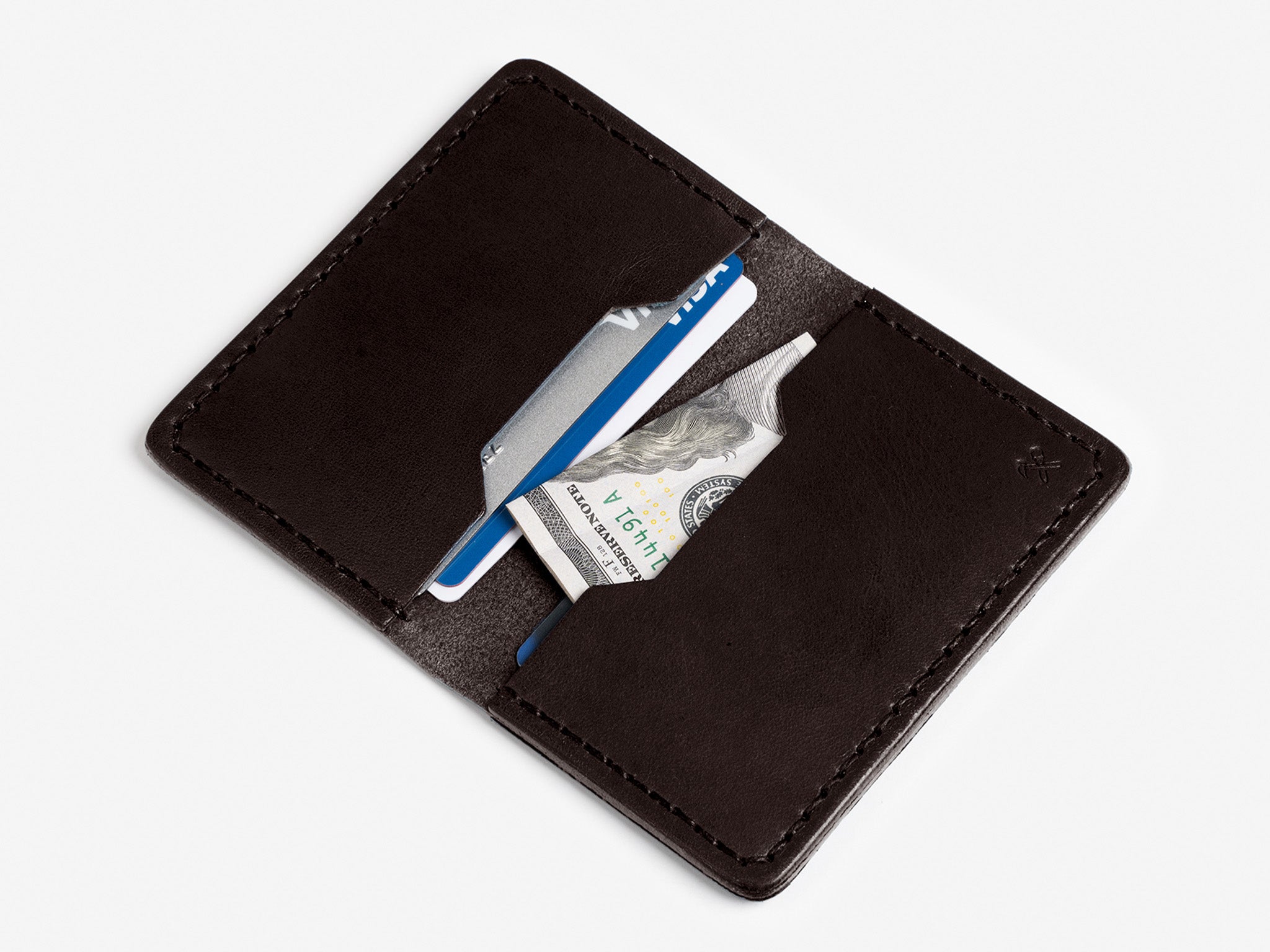 An open dark brown leather wallet with two card slots, containing two credit cards and a folded U.S. dollar bill, displayed on a white background.