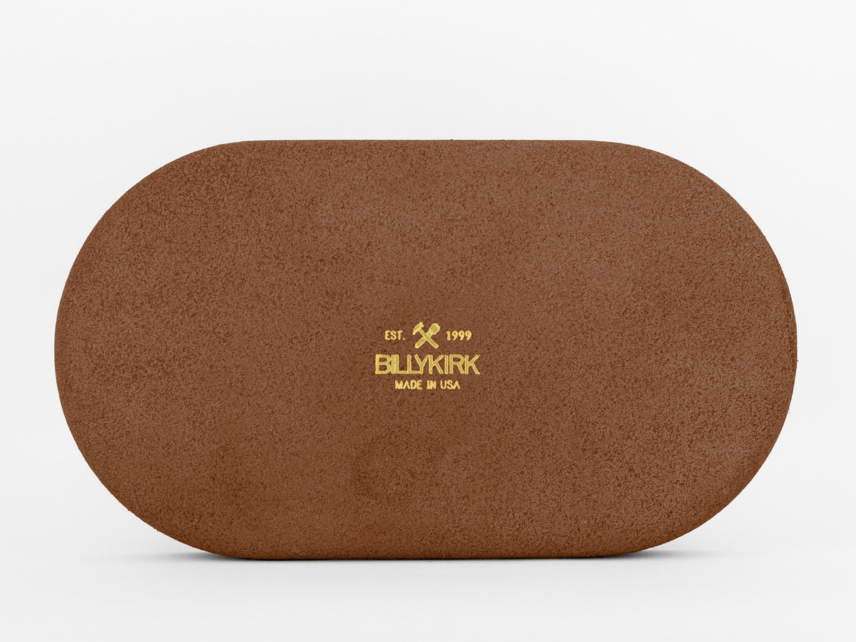 A brown, oval leather object with gold text in the center reading Est. 1999 BLUKIRK MADE IN USA, displayed against a plain white background.