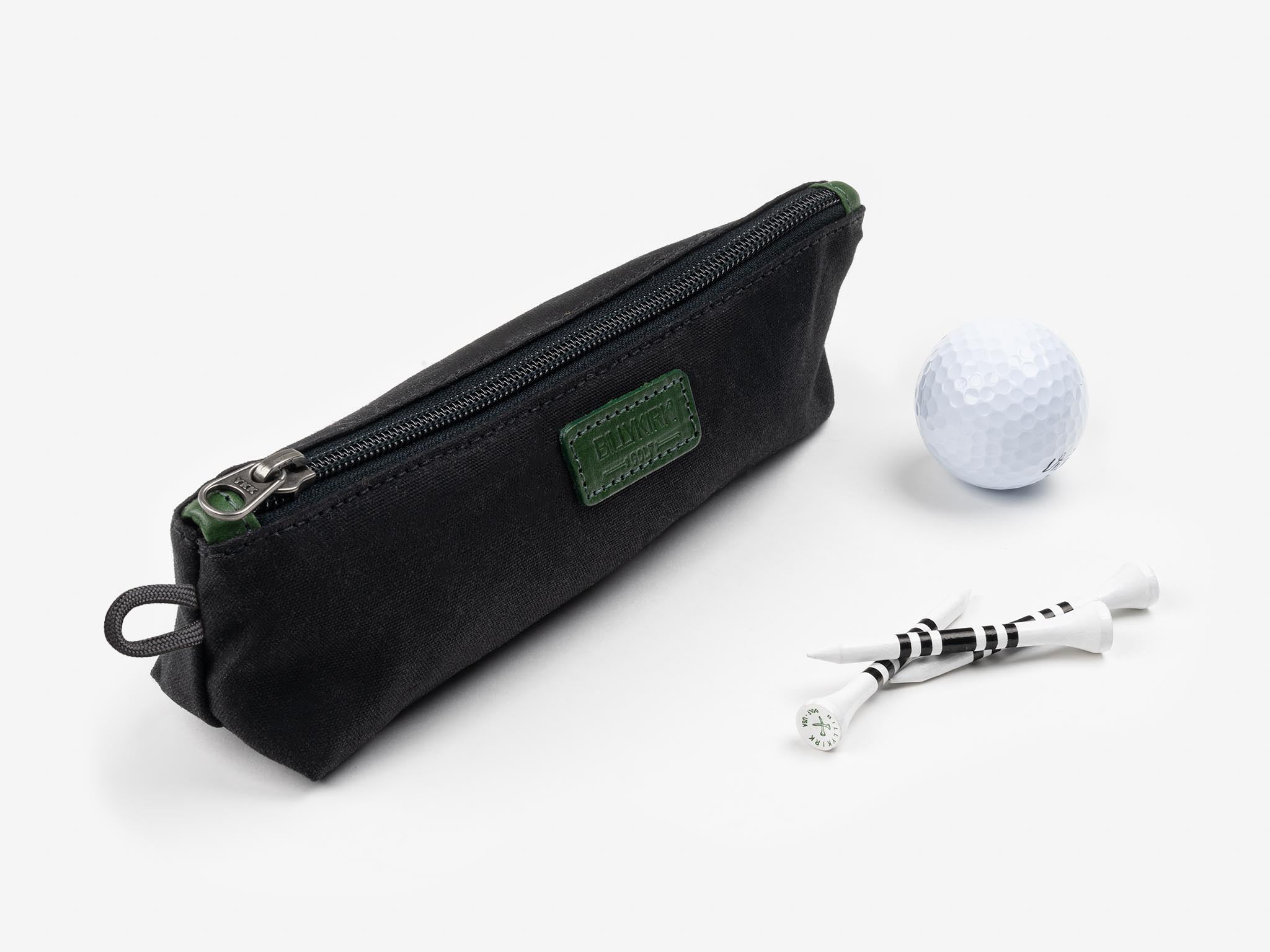 A black zippered pouch, a white golf ball, and three white golf tees with black stripes arranged on a white surface.
