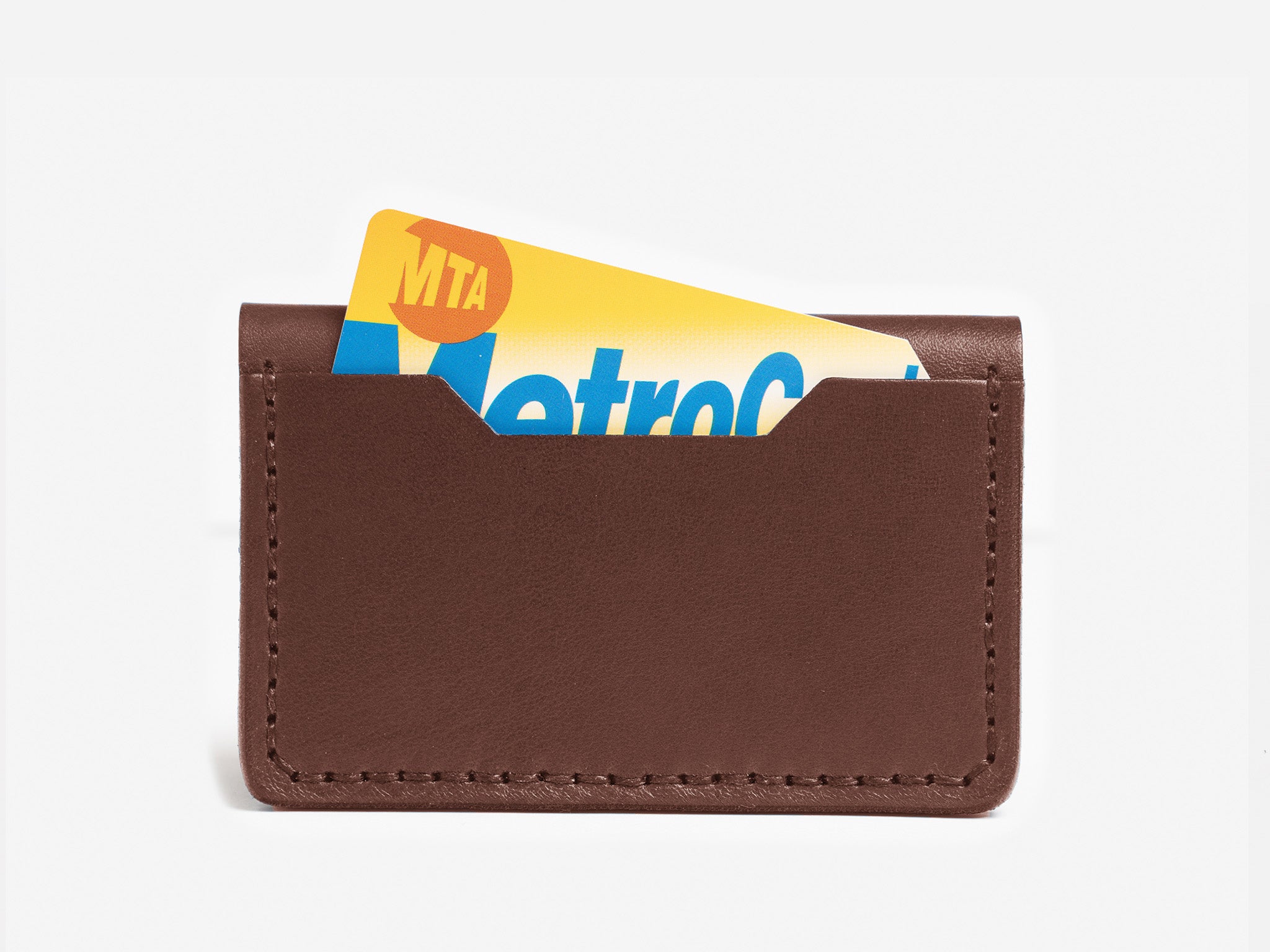 A brown leather card holder with an MTA MetroCard partially visible inside, set against a plain white background.