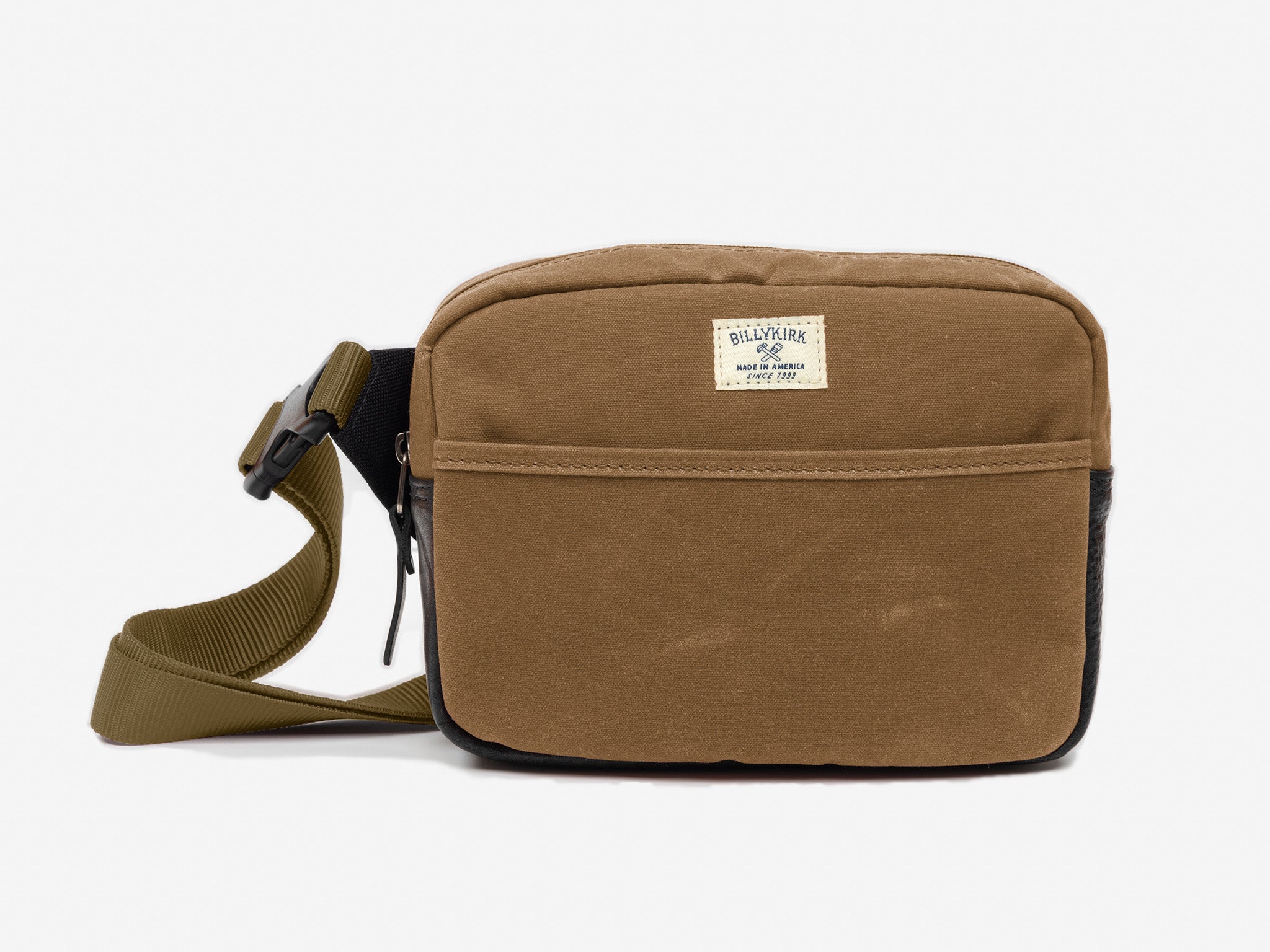 A small brush brown waxed canvas crossbody bag with a front pocket, adjustable strap, and a cream colored rectangular Billykirk brand patch stitched on the front.