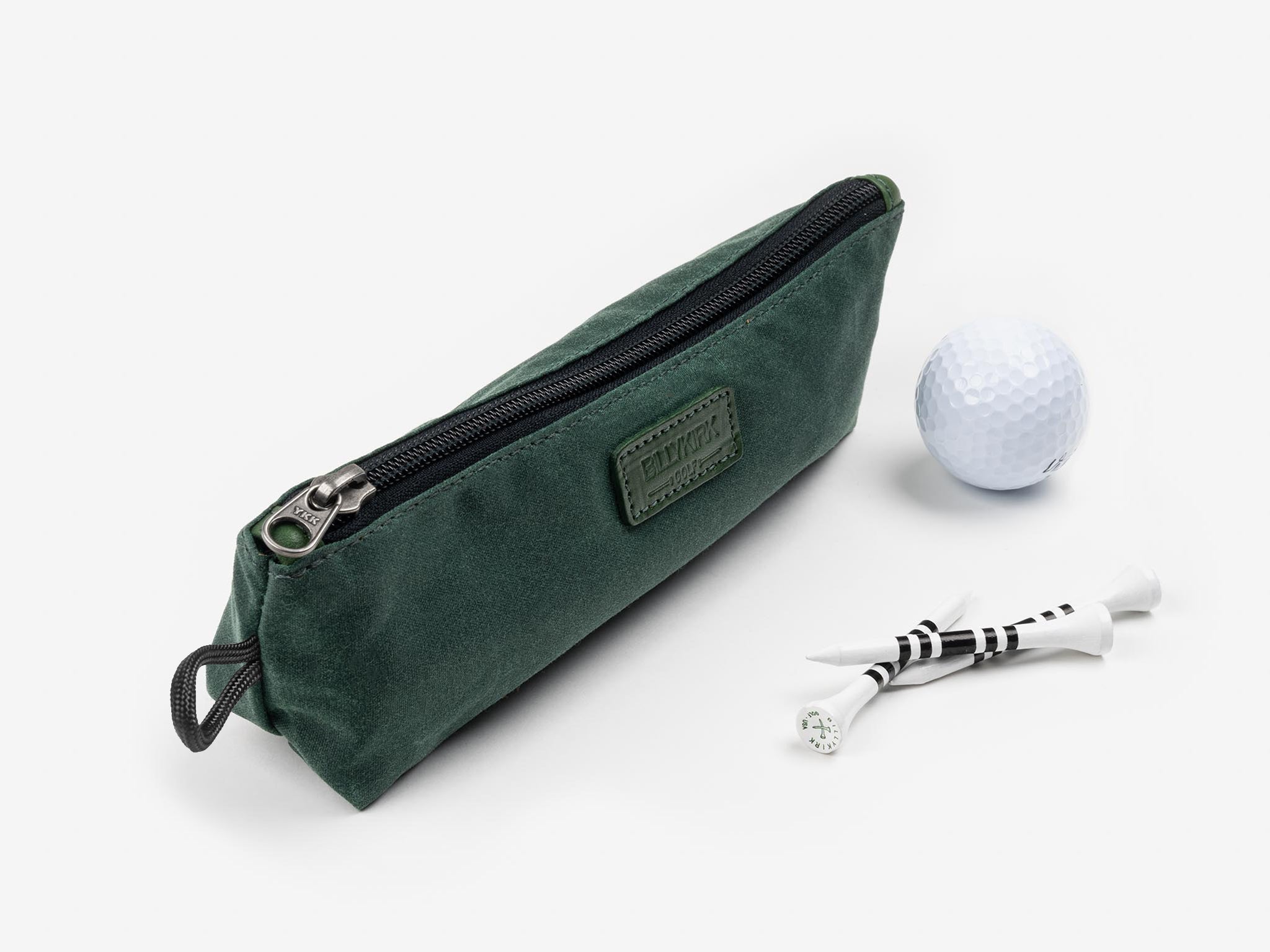 A green zippered pouch is shown next to a white golf ball and four white golf tees with black stripes, all set against a plain white background.