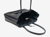 A black leather tote resting on its side, open. It features an interior organization pocket and a removable luggage tag set with a neutral background.